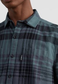 Kariertes Flanellhemd in Türkis, Schwarz und Dunkelgrau. Mit Knopfleiste, zwei Brusttaschen und einem Etikett mit dem Markennamen O'Neill.