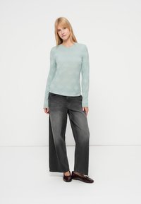 Ανοιχτό τιρκουάζ μακρυμάνικο τοπ με υφασμένο λουλουδένιο μοτίβο, συνδυασμένο με άνετα σκούρα γκρι τζιν και μπορντό μπαλαρίνες.