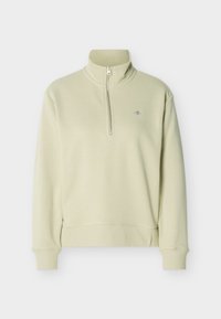 Ανοιχτό μπεζ πουλόβερ με φερμουάρ μέχρι το στήθος, γιακά τύπου στάντ, ριμπ μανσέτες και τελείωμα, και μικρό κεντημένο λογότυπο στο αριστερό μέρος του στήθους.