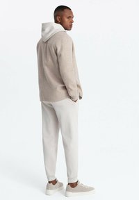Veste en polaire beige clair avec une capuche blanche, associée à un pantalon grisé tapered clair et des baskets en daim, vue de dos.