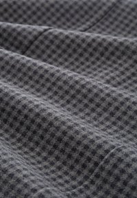Tissu gris à motif avec une surface texturée, présentant un petit design géométrique en gris foncé, montrant plis et profondeur.