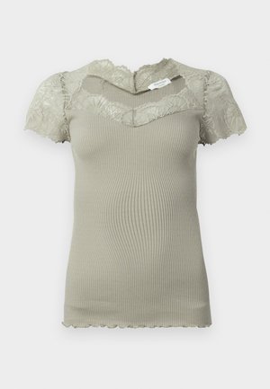 Lyhyt beige ribbikudos toppi, jossa on pitsiyksityiskohtia kaula-aukossa ja lyhyissä hihoissa, sekä sahalaitaiset reunat hihoissa ja helmassa.