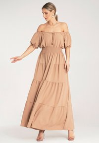 Sukienka maxi w jasnobrązowym materiale, fason bez ramiączek, gumowany pas, krótkie bufiaste rękawy, warstwowa spódnica oraz drewniane guziki jako akcenty.