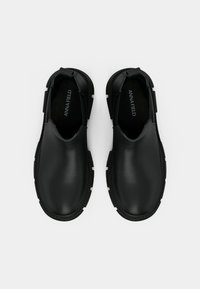 Pár čiernych šľapiek s hrubou podrážkou a hladkým povrchom, s označením "ANNA FIELD" vo vnútri, zobrazený zhora na bielom pozadí.