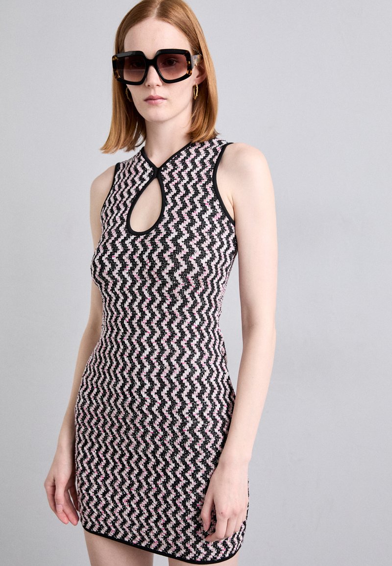 Knit dress with a zigzag pattern in black, pink, and white. Features a fitted silhouette and a keyhole neckline. Black trim around edges.