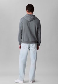 Felpa grigia con tasca a marsupio, polsini e orlo a coste. Abbinata a jeans in denim chiaro e sneaker bianche.
