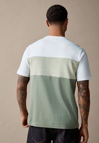 Rövid ujjú póló színblokkolt mintával, fehér, világoszöld és sötétzöld részekkel, puha pamut anyagból készült.