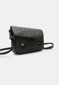 Borsa nera con superficie testurizzata, decorata con borchie metalliche. Presenta una chiusura a soffietto e una tracolla regolabile.