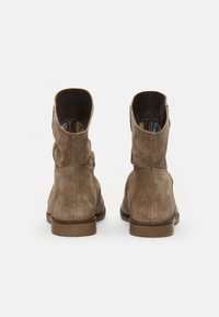 Bottines en daim marron avec un petit talon, présentant un bout arrondi et des coutures apparentes ; l'intérieur montre un doublage en textile coloré.