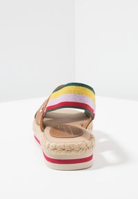 Sandale en cuir marron avec une bande en tissu rayé multicolore comportant du jaune, du vert, du rose et du rouge. Semelle en jute de style espadrille.