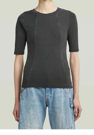 Osoba ubrana w dopasowaną ciemnoszarą prążkowaną koszulkę z krótkim rękawem z widocznymi szwami oraz jasnobeżowe jasnoniebieskie szorty dżinsowe z bocznymi kieszeniami.