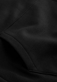 Primo piano di un tessuto nero caratterizzato da una texture morbida con cuciture visibili, bordi curvi e una superficie liscia priva di motivi o elementi hardware.