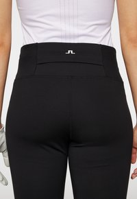 Svart atletiska leggings med hög midja, med en liten vit logotyp på baksidan, slät textur och minimala sömnadsdetaljer.