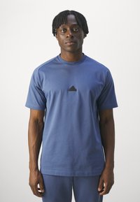 Niebieska koszulka z krótkim rękawem, wykonana z miękkiego materiału, z małym czarnym logo Adidas na piersi i okrągłym dekoltem. Prosty design.