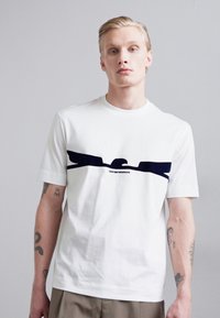 Witte katoenen T-shirt met een zwart grafisch ontwerp over de borst. Korte mouwen, normale hals en een relaxed fit.