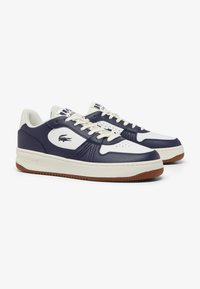 Zapatillas Lacoste con parte superior en cuero azul marino, acentos blancos, un diseño texturizado y suela de goma. Presentan cierre con cordones y logotipo.