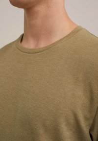Suéter de punto texturizado en verde oliva con cuello redondo. La tela presenta un patrón sutil y elevado, además de una textura suave y transpirable.