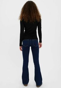 Un haut noir à manches longues associé à un jean évasé bleu marine, mettant en avant un tissu lisse et une coupe ajustée, avec de subtils détails sur les poches arrière.