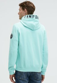 Felpa verde menta con cordino, caratterizzata da un'etichetta stampata "CAMP DAVID" nera sul colletto e un'etichetta con logo circolare sulla manica.