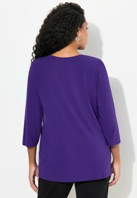 Pitkähihaine violetti paita, jossa on pyöreä kaula-aukko, sileä rakenne, rento istuvuus ja 3/4-hihat, yhdistetty mustiin housuihin.