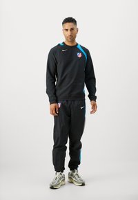 Sort sweatshirt med blå detaljer, der har et logo og rund halsudskæring. Sorte bukser med en blå stribe, parret med multicolor træningssko.