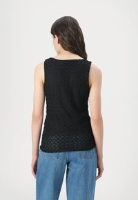 Top preto sem mangas com um padrão texturizado e tecido, e decote arredondado, combinado com jeans de perna larga azul claro.