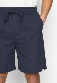 Pantalones cortos azul marino hechos de tela texturizada, que cuentan con una cinturilla elástica con cordón y bolsillos laterales.