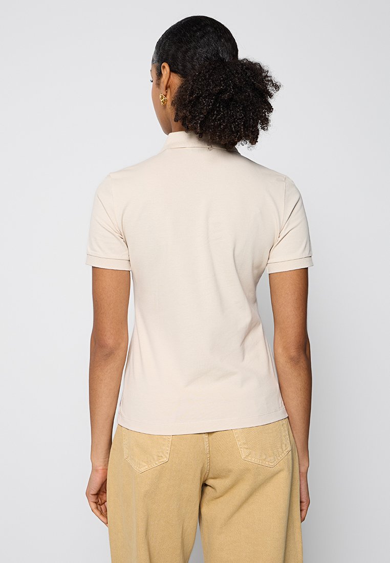 Helles beiges Polohemd mit kurzen Ärmeln, aus weichem Baumwollmaterial, klassischem Kragen und minimalistischem Design. Tragen mit beigen Hosen, die eine entspannte Passform zeigen.