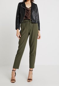 Svart läderbikerjacka i lager över en leopardmönstrad cami, tillsammans med högt skurna olivgröna byxor och remsandaler i brunt.