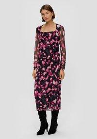 Langemouwige jurk met vierkante hals in doorzichtig zwart materiaal met een roze en paarse abstracte print en een aansluitende silhouet, gecombineerd met hoge zwarte laarzen tot de knie.