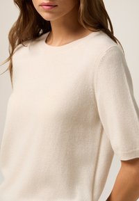 Beige kortemouwen trui gemaakt van een zachte, gestructureerde stof met een ronde halslijn en een relaxte pasvorm, met delicate ribbelaccenten bij de naden.