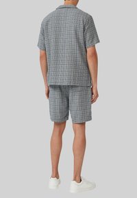 Korte mouw knoopshirt en bijpassende shorts in een textuurpatroon van blauw en wit, gecombineerd met witte sneakers.