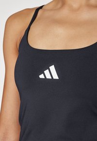 Zwarte sportieve tanktop met een wit driehoekig logo. De stof lijkt glad met smalle bandjes en een ronde halslijn.