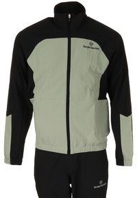 Completo sportivo da uomo caratterizzato da un design a blocchi di colore nero e verde chiaro, realizzato in tessuto leggero, con giacca con zip e vita elastica.