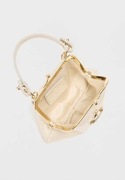 Μικρή τσάντα χειρός σε κρεμ χρώμα με χρυσό μεταλλικό σκελετό και κούμπωμα, με έναν ιμάντα καρπού, ανοιχτή με ορατή μπεζ επένδυση στο εσωτερικό.