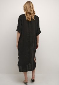 Abito in lino nero con vestibilità ampia, maniche arrotolabili, fessure laterali e lunghezza sotto il ginocchio. Tessuto leggero, design semplice.