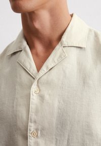 Helles beige Leinenhemd mit einem Notchkragen, drei Knöpfen und einem strukturierten Stoff für eine lässige Silhouette.