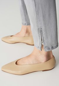 Ballerines beiges à bout-pointu avec une finition en cuir lisse. Jeans gris avec une fermeture éclair sur le côté à la cheville pour un ajustement réglable.
