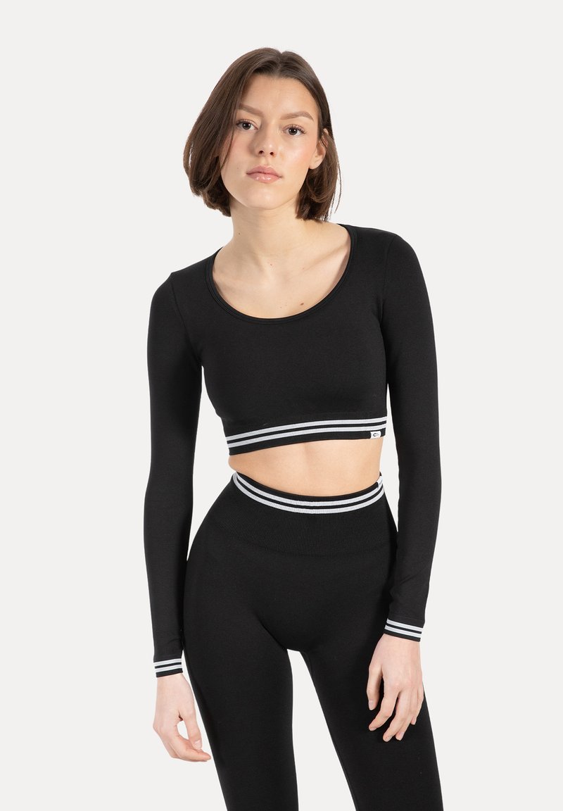 Czarny krótki top z długim rękawem z białym paskiem w paski u dołu, w połączeniu z czarnymi legginsami z wysokim stanem z pasującymi paskami na pasie.