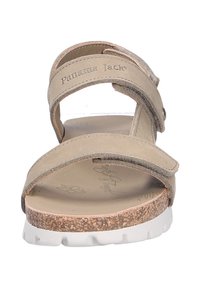 Sandalia beige con dos correas ajustables, plantilla de corcho y suela de goma blanca. Presenta un logotipo grabado en la correa y un diseño plano.