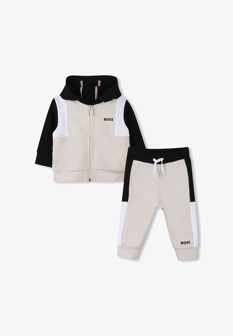 Tvådelad träningsdräkt i beige, svart och vitt. Innehåller en zip-up huvtröja och tapered byxor med kontrasterande färgblock och logodetalj.