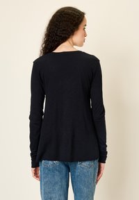 Must pikkade varrukatega pluus, lõdvaistmeline, veidi kaardus äärega ja pehme tekstuuriga, kombineeritud helesiniste kõrge vöökohaga teksadega.