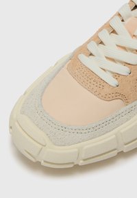Baskets beiges et gris clair avec des panneaux en cuir suédé texturé et en synthétique lisse. Elles disposent d'une épaisse semelle crème et de lacets blancs.