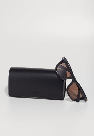 Black sunglasses with brown lenses, featuring a geometric design and gold accents, resting on a black leather case embossed with "Zegna."