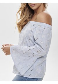 Blusa blu off-the-shoulder con motivi floreali ricamati bianchi, maniche a campana e tessuto testurizzato. Design casual adatto per il clima caldo.