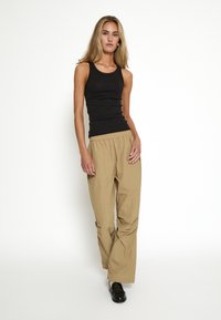 Canotta nera aderente abbinata a pantaloni cargo beige con vita elastica, caratterizzati da una vestibilità comoda e una texture di tessuto liscia. Scarpe nere completano l'outfit.