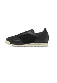 Schwarzer Sportschuh mit strukturiertem Obermaterial, drei schwarzen Streifen und einer kontrastierenden beigen Außensohle mit Zickzackmuster.