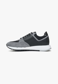 Heren sneaker in zwart en grijs suede en leer, met een gestructureerde bovenkant, zwarte mesh accenten en een witte ribbelrubberen zool.