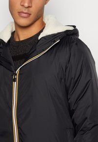 Giacca nera con cappuccio, foderata in morbido pile bianco, dotata di chiusura a zip con un accento a strisce colorate lungo la zip.