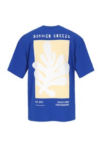 Blauwe katoenen t-shirt met een grote witte abstracte bladerenafbeelding op een pastelgele achtergrond, met logo-tekst erboven en eronder.